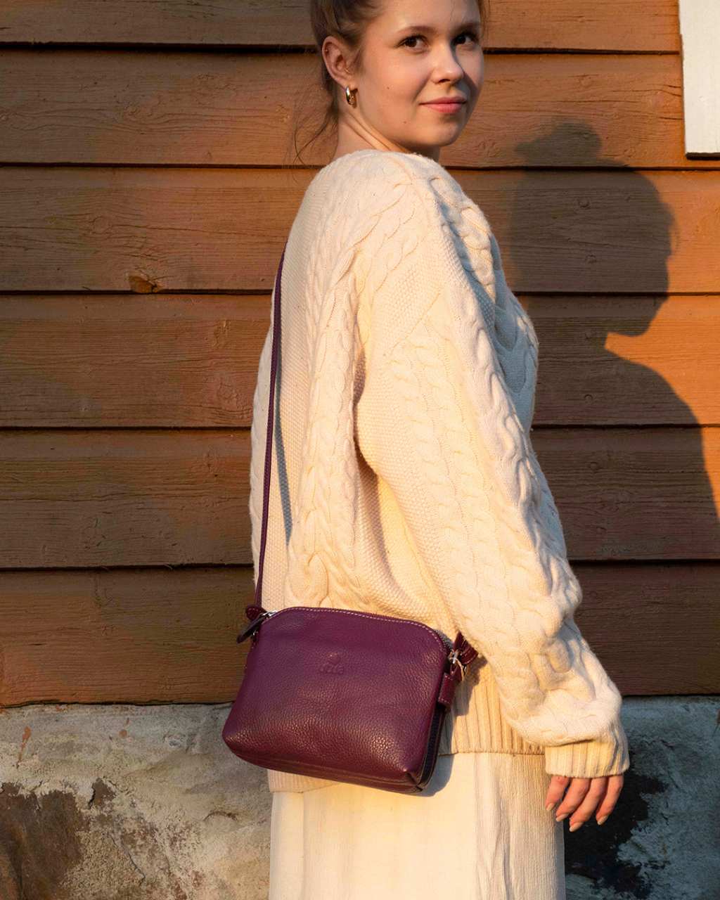 utua-tumman-violetti-lysti-pikkulaukku-talon-seinustalla